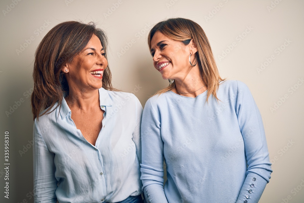 Middle age beautiful couple of sisters standing over isolated white background looking away to side with smile on face, natural expression. Laughing confident. Middle age beautiful couple of sisters standing over isolated white background looking away to side with smile on face, natural expression. Laughing confident.