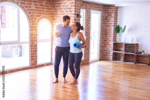 Middle age beautiful sporty couple smiling happy. Standing with smile on face hugging and holding mat at gym