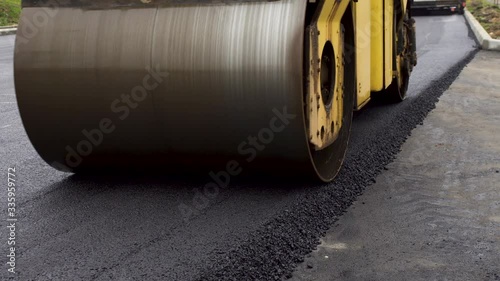 A large yellow steamroller flatten hot asphalt. Builds a new road