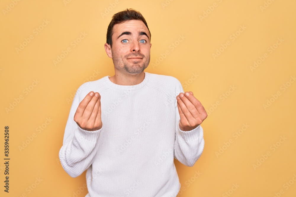 Young handsome man with blue eyes wearing casual sweater standing over yellow background doing money gesture with hands, asking for salary payment, millionaire business Young handsome man with blue eyes wearing casual sweater standing over yellow background doing money gesture with hands, asking for salary payment, millionaire business