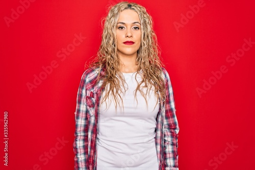 Young beautiful blonde woman wearing casual shirt standing over isolated red background Relaxed with serious expression on face. Simple and natural looking at the camera.