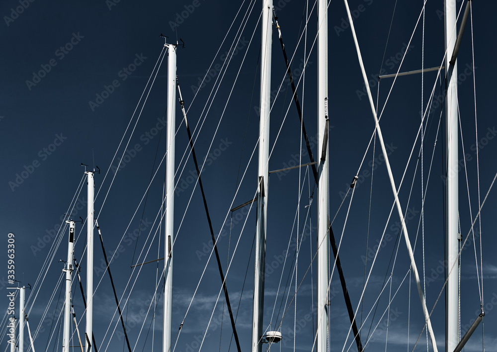 Obraz premium The number of masts of sailboats with the blue sky on a background, a sail regatta, reflection of masts on water, ropes and aluminum, Bright colors