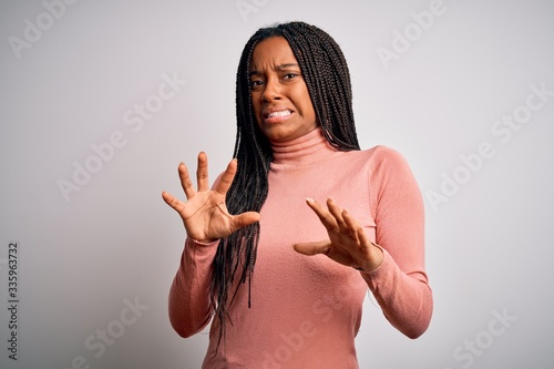 Young african american woman standing casual and cool over white isolated background disgusted expression, displeased and fearful doing disgust face because aversion reaction. With hands raised