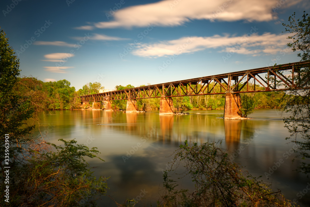 Obraz premium A long exposure of a train trestle over a river with a blue sky.