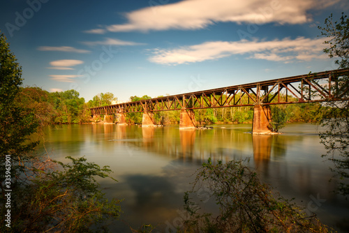 A long exposure of a train trestle over a river with a blue sky.