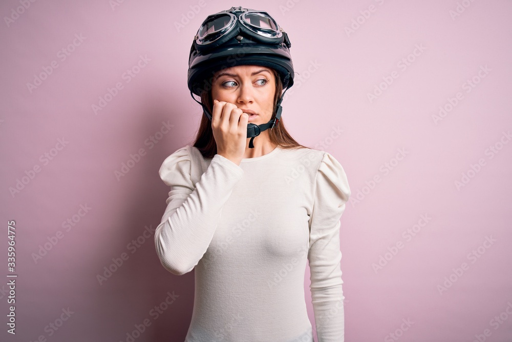 Young beautiful motorcyclist woman with blue eyes wearing moto helmet over pink background looking stressed and nervous with hands on mouth biting nails. Anxiety problem. Young beautiful motorcyclist woman with blue eyes wearing moto helmet over pink background looking stressed and nervous with hands on mouth biting nails. Anxiety problem.