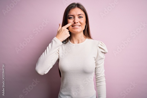 Young beautiful woman with blue eyes wearing casual white t-shirt over pink background Pointing with hand finger to face and nose, smiling cheerful. Beauty concept