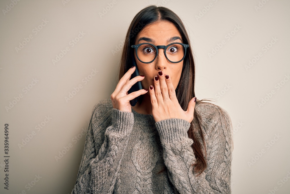 Young beautiful brunette woman wearing glasses having conversation talking on smartphone cover mouth with hand shocked with shame for mistake, expression of fear, scared in silence, secret concept Young beautiful brunette woman wearing glasses having conversation talking on smartphone cover mouth with hand shocked with shame for mistake, expression of fear, scared in silence, secret concept