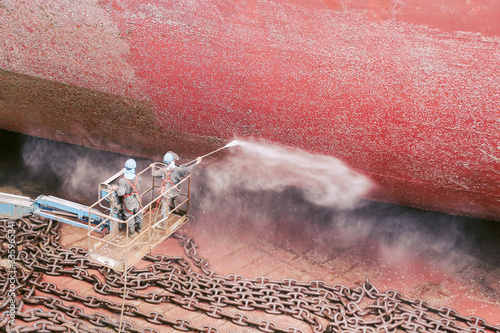 Top view worker under ship washing cleaning by high pressure gun water at floating drydock in shipyard ship with anchor chain on floor