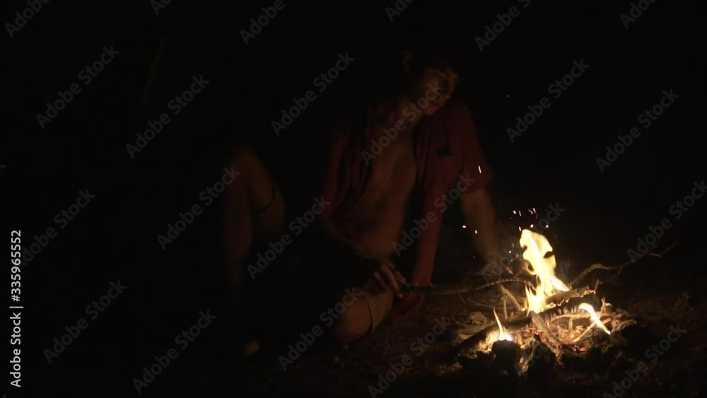 Alone man sitting in front of the campfire in the dark. Summer camping in a tropical place. Slow motion.