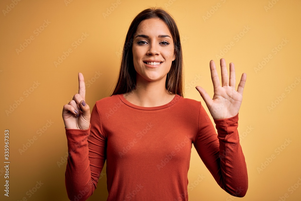 Young beautiful brunette woman wearing casual t-shirt standing over yellow background showing and pointing up with fingers number six while smiling confident and happy. Young beautiful brunette woman wearing casual t-shirt standing over yellow background showing and pointing up with fingers number six while smiling confident and happy.