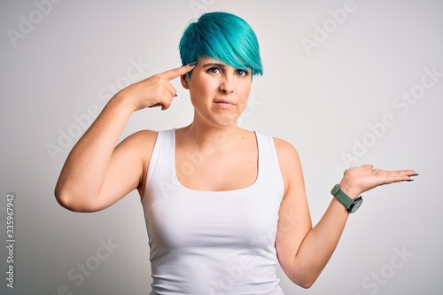 Young beautiful woman with blue fashion hair wearing casual t-shirt over white background confused and annoyed with open palm showing copy space and pointing finger to forehead. Think about it. © Krakenimages.com