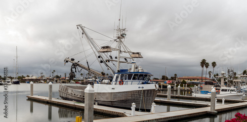 Fényképezés Harbor docks in Ventura sit over calm water with squid fishing boat moored under overcast cloudy sky