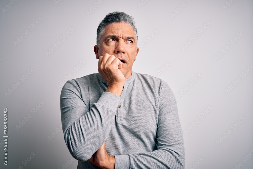 Middle age handsome grey-haired man wearing casual t-shirt over white background looking stressed and nervous with hands on mouth biting nails. Anxiety problem.