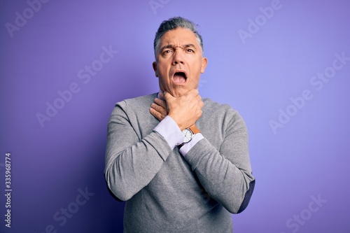Middle age handsome grey-haired man wearing elegant sweater over purple background shouting and suffocate because painful strangle. Health problem. Asphyxiate and suicide concept.