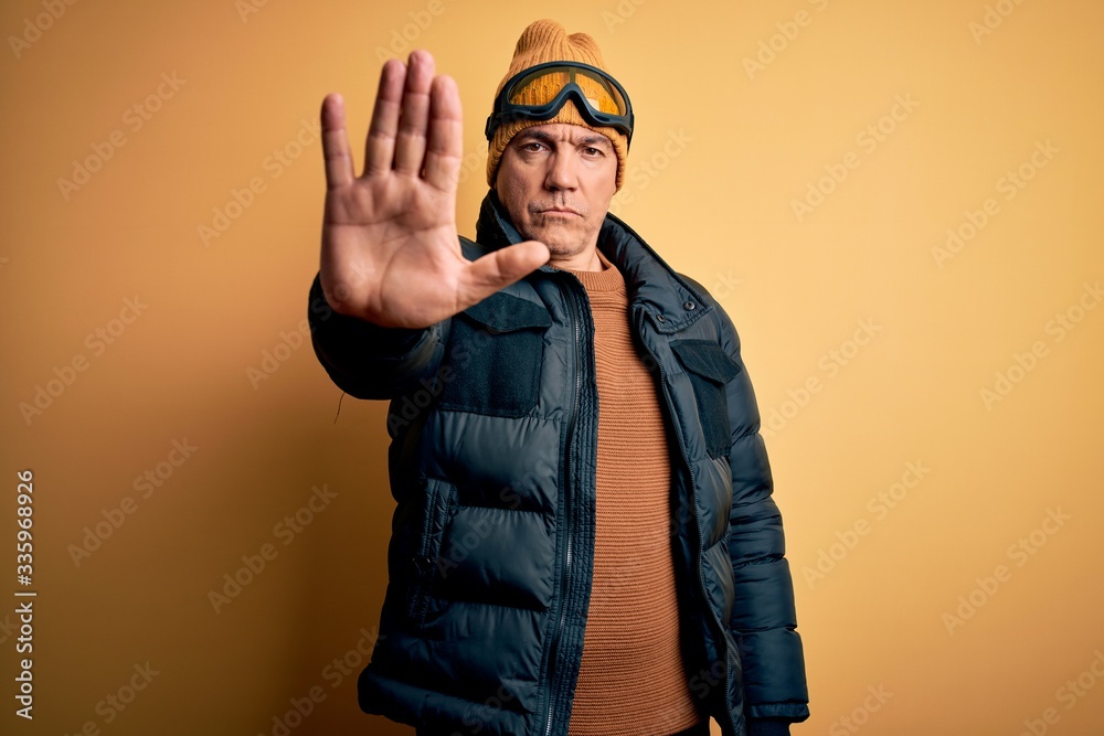 Middle age handsome grey-haired skier man on vacation wearing ski goggles doing stop sing with palm of the hand. Warning expression with negative and serious gesture on the face. Middle age handsome grey-haired skier man on vacation wearing ski goggles doing stop sing with palm of the hand. Warning expression with negative and serious gesture on the face.