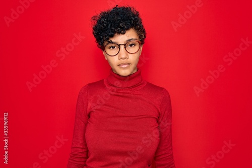 Young beautiful african american afro woman wearing turtleneck sweater and glasses Relaxed with serious expression on face. Simple and natural looking at the camera. © Krakenimages.com