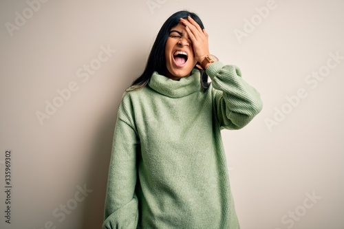 Young beautiful hispanic woman wearing green winter sweater over isolated background Yawning tired covering half face, eye and mouth with hand. Face hurts in pain. © Krakenimages.com