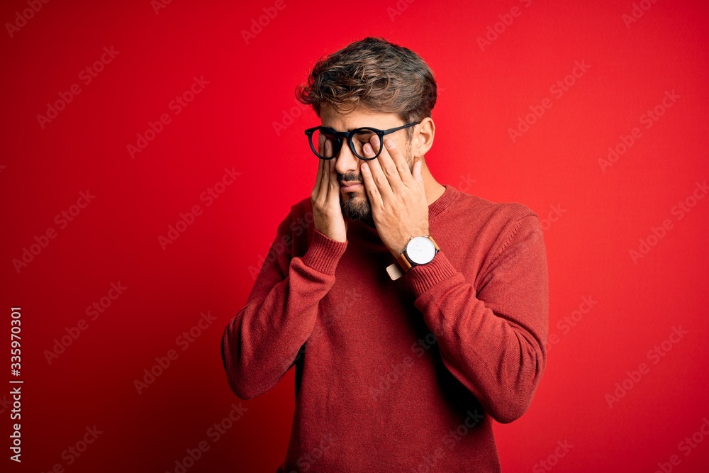 © Krakenimages.com - Young handsome man with beard wearing glasses and sweater standing over red background rubbing eyes for fatigue and headache, sleepy and tired expression. Vision problem