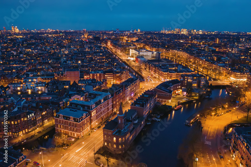 Aerial panoramic view of evening Amsterdam with water canals  illuminated roads and historic buildings  The Netherlands.