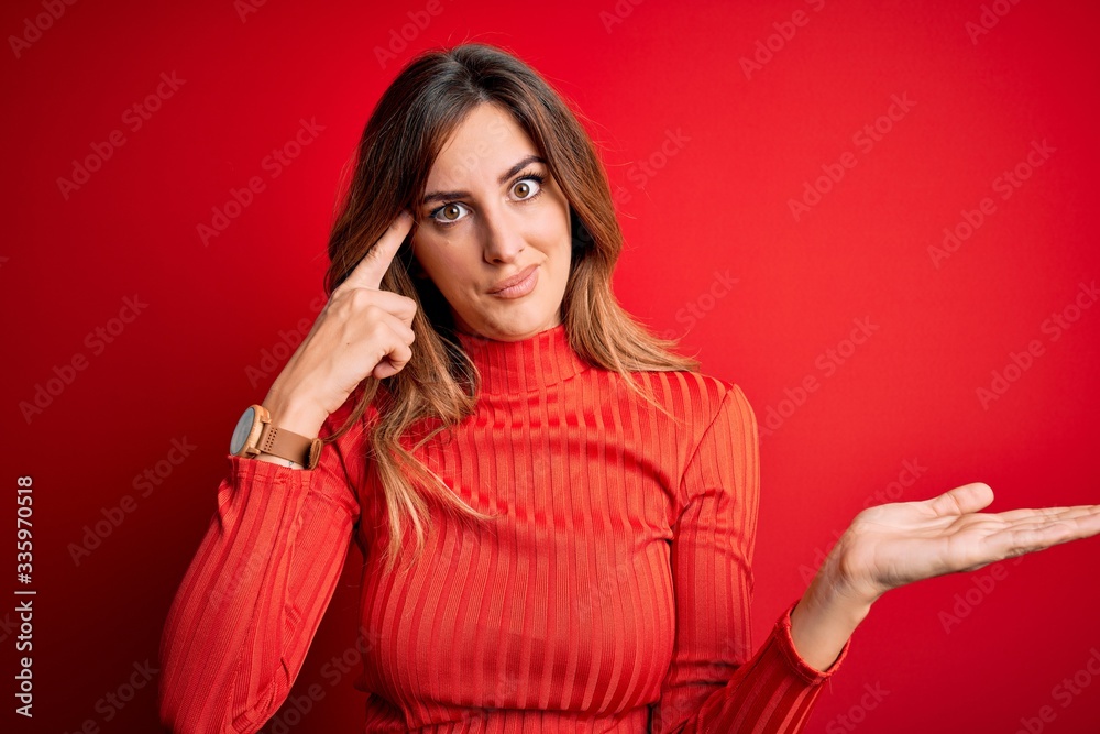 Young beautiful brunette woman wearing casual turtleneck sweater over red background confused and annoyed with open palm showing copy space and pointing finger to forehead. Think about it. Young beautiful brunette woman wearing casual turtleneck sweater over red background confused and annoyed with open palm showing copy space and pointing finger to forehead. Think about it.