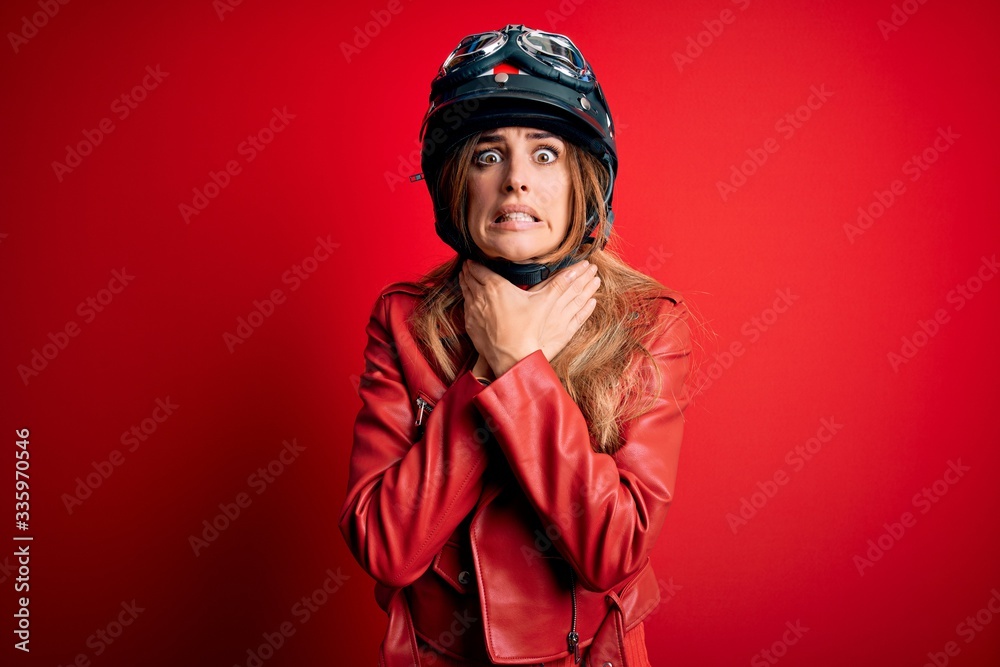 Young beautiful brunette motrocyclist woman wearing moto helmet over red background shouting and suffocate because painful strangle. Health problem. Asphyxiate and suicide concept. Young beautiful brunette motrocyclist woman wearing moto helmet over red background shouting and suffocate because painful strangle. Health problem. Asphyxiate and suicide concept.