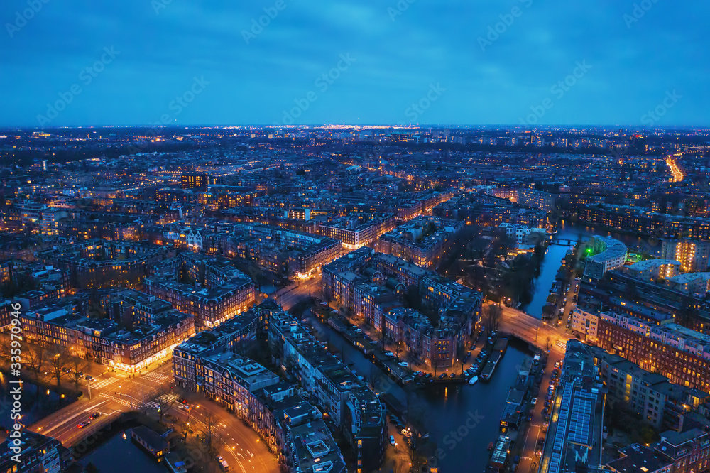 Aerial panoramic view of evening Amsterdam with water canals, illuminated roads and historic buildings, The Netherlands.