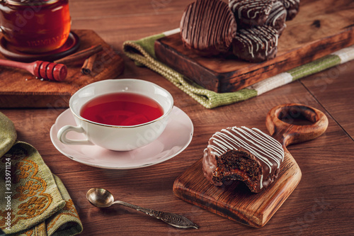 A bitten honey cookie chocolate covered on the wooden table with a porcelain cup of tea, honey bee and cinnamon - pão de mel