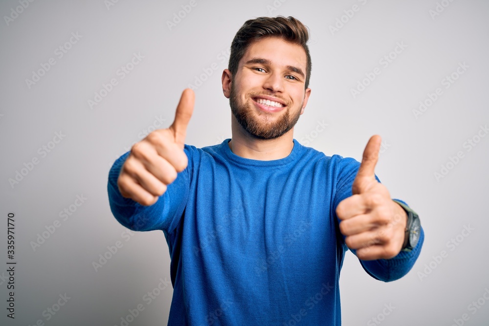 Young handsome blond man with beard and blue eyes wearing casual sweater approving doing positive gesture with hand, thumbs up smiling and happy for success. Winner gesture. Young handsome blond man with beard and blue eyes wearing casual sweater approving doing positive gesture with hand, thumbs up smiling and happy for success. Winner gesture.