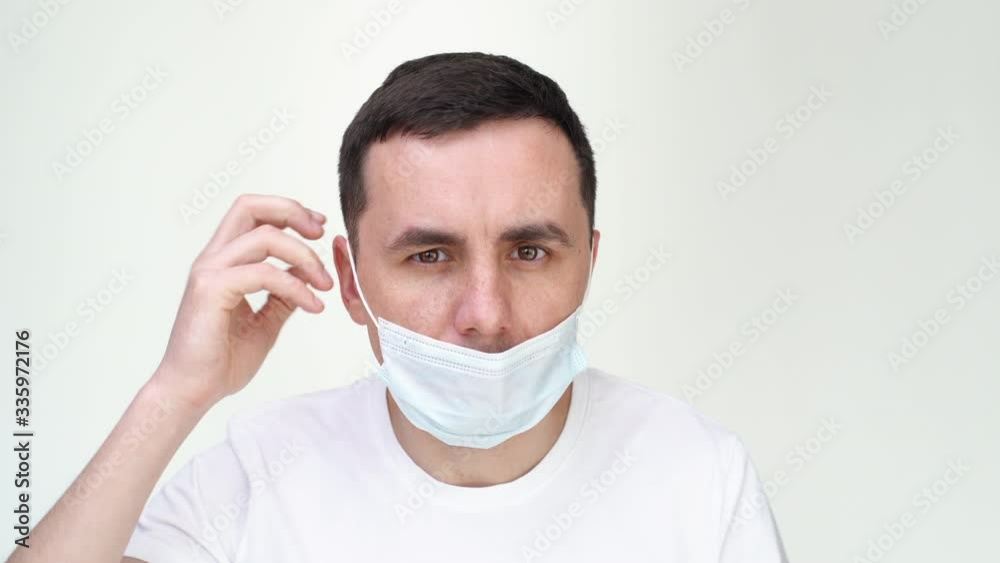 Close-up of face of young man putting medical mask and looking at the camera on white isolated background. Prevention of virus infection. Concept of Coronavirus COVID-19 Pandemic.
