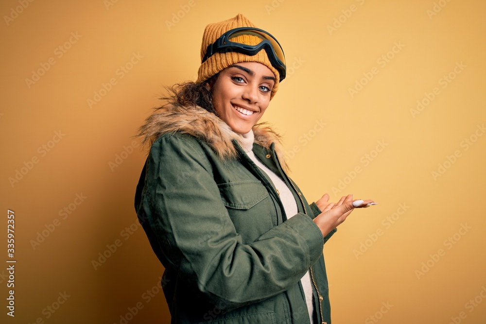 Young african american afro skier girl wearing snow sportswear and ski goggles Inviting to enter smiling natural with open hand Young african american afro skier girl wearing snow sportswear and ski goggles Inviting to enter smiling natural with open hand