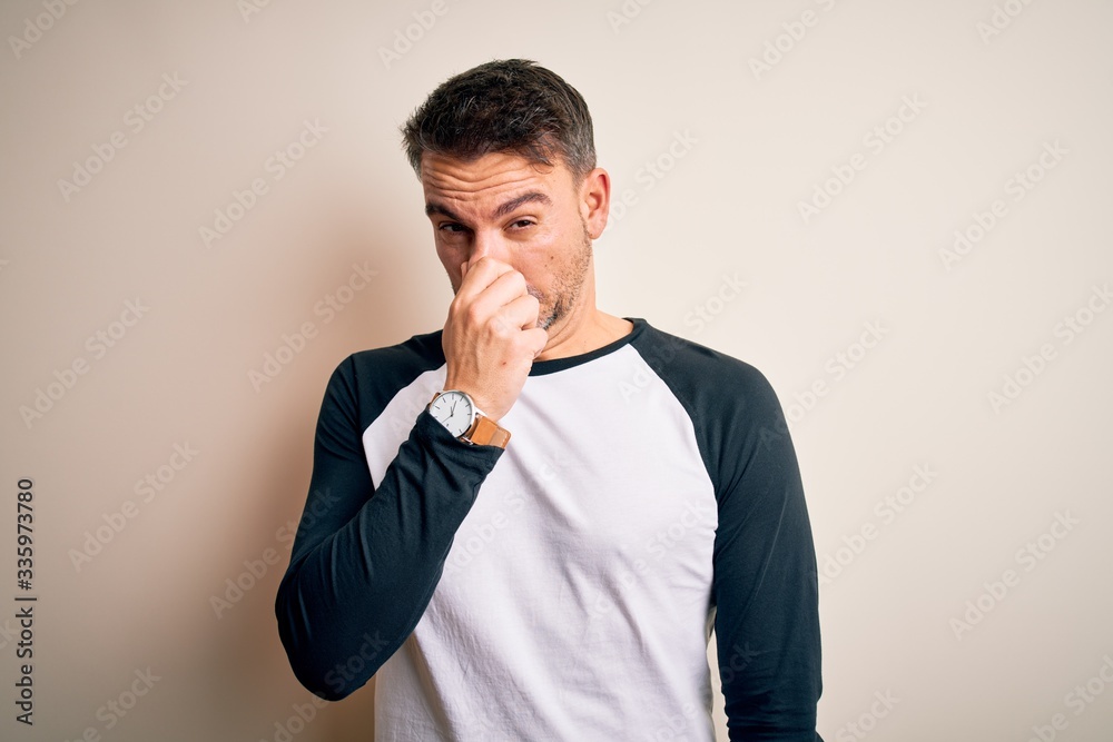Young handsome man wearing casual t-shirt standing over isolated white background smelling something stinky and disgusting, intolerable smell, holding breath with fingers on nose. Bad smell Young handsome man wearing casual t-shirt standing over isolated white background smelling something stinky and disgusting, intolerable smell, holding breath with fingers on nose. Bad smell