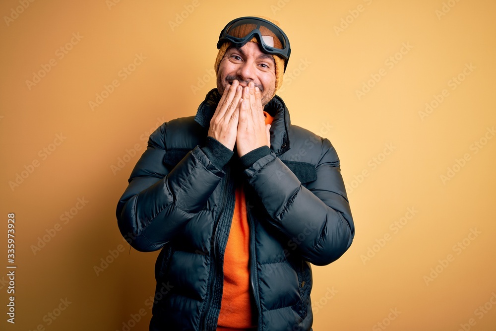 Young handsome skier man skiing wearing snow sportswear using ski goggles laughing and embarrassed giggle covering mouth with hands, gossip and scandal concept Young handsome skier man skiing wearing snow sportswear using ski goggles laughing and embarrassed giggle covering mouth with hands, gossip and scandal concept