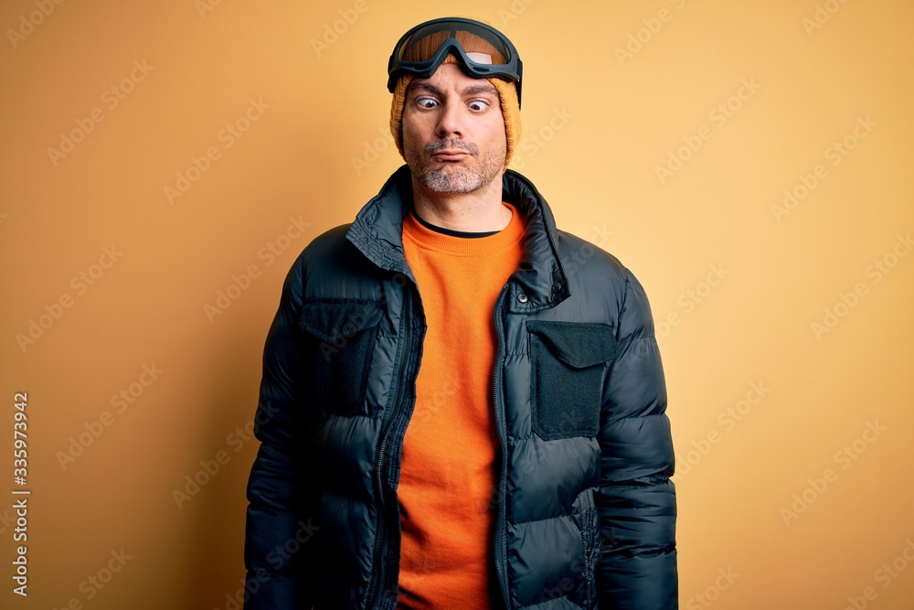 Young handsome skier man skiing wearing snow sportswear using ski goggles making fish face with lips, crazy and comical gesture. Funny expression. Young handsome skier man skiing wearing snow sportswear using ski goggles making fish face with lips, crazy and comical gesture. Funny expression.