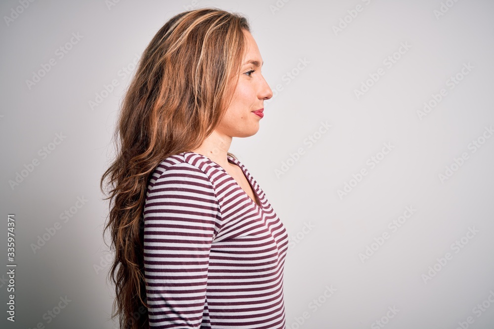 Young beautiful blonde woman wearing casual striped t-shirt over isolated white background looking to side, relax profile pose with natural face with confident smile. Young beautiful blonde woman wearing casual striped t-shirt over isolated white background looking to side, relax profile pose with natural face with confident smile.