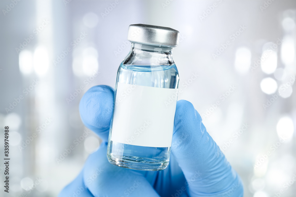 Healthcare concept with a hand in blue medical gloves holding a vaccine vial with blue liquid and black white label Healthcare concept with a hand in blue medical gloves holding a vaccine vial with blue liquid and black white label