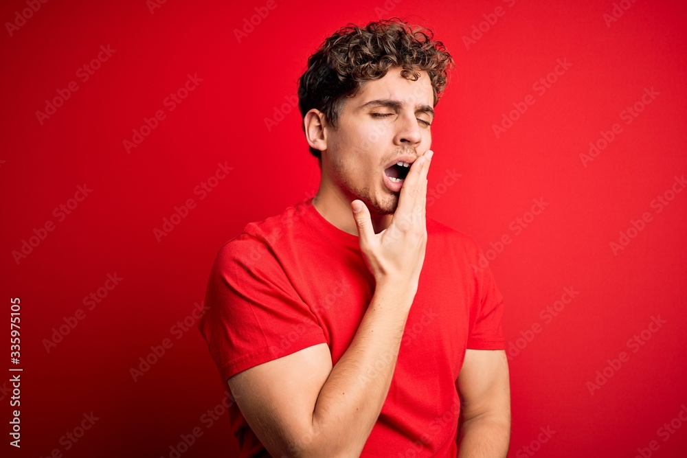 Young blond handsome man with curly hair wearing casual t-shirt over red background bored yawning tired covering mouth with hand. Restless and sleepiness. Young blond handsome man with curly hair wearing casual t-shirt over red background bored yawning tired covering mouth with hand. Restless and sleepiness.