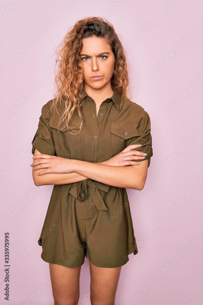 Young beautiful woman with blue eyes wearing casual summer dress over pink background skeptic and nervous, disapproving expression on face with crossed arms. Negative person. Young beautiful woman with blue eyes wearing casual summer dress over pink background skeptic and nervous, disapproving expression on face with crossed arms. Negative person.