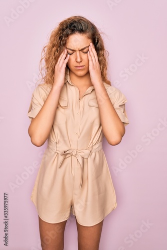 Young beautiful woman with blue eyes wearing casual summer dress over pink background suffering from headache desperate and stressed because pain and migraine. Hands on head.