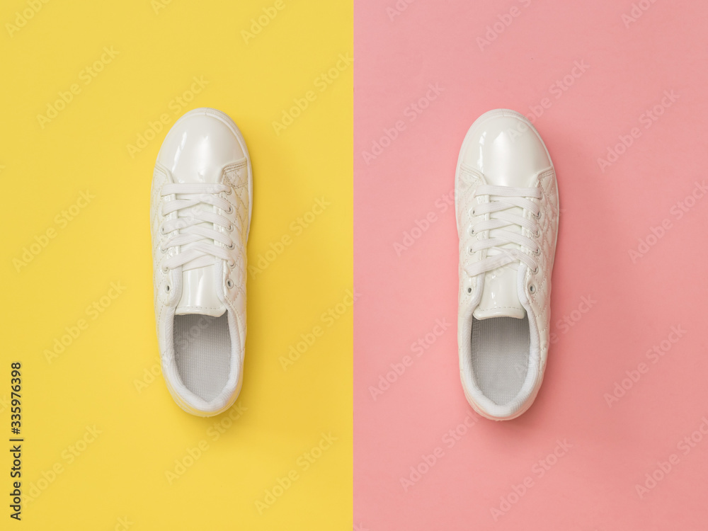 White athletic sneakers on a pink and yellow background. Sports style. Flat lay. White athletic sneakers on a pink and yellow background. Sports style. Flat lay.