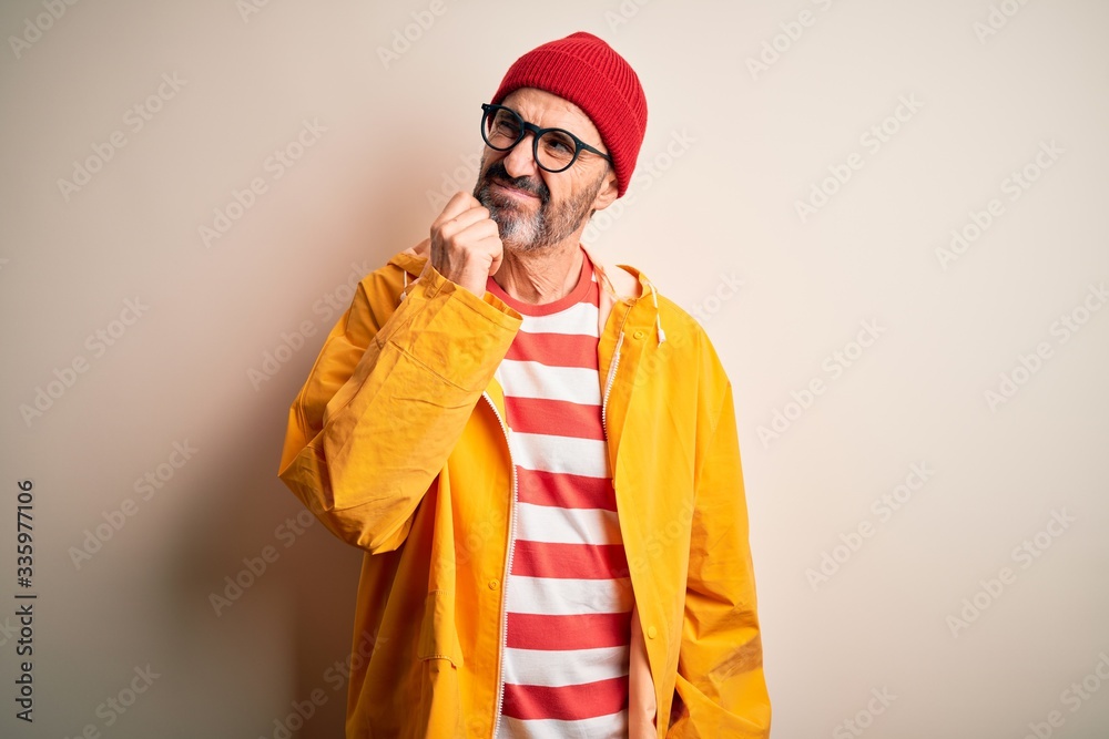 Middle age hoary man wearing glasses and rain coat standing over isolated white background with hand on chin thinking about question, pensive expression. Smiling with thoughtful face. Doubt concept.