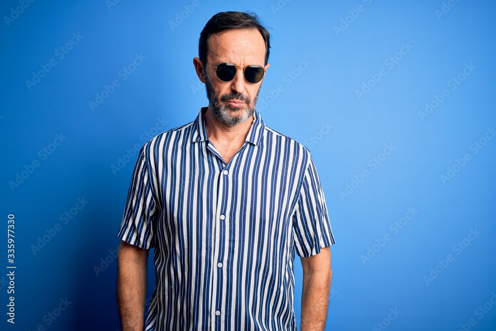 Middle age hoary man wearing striped shirt and sunglasses over isolated blue background skeptic and nervous, frowning upset because of problem. Negative person. Middle age hoary man wearing striped shirt and sunglasses over isolated blue background skeptic and nervous, frowning upset because of problem. Negative person.