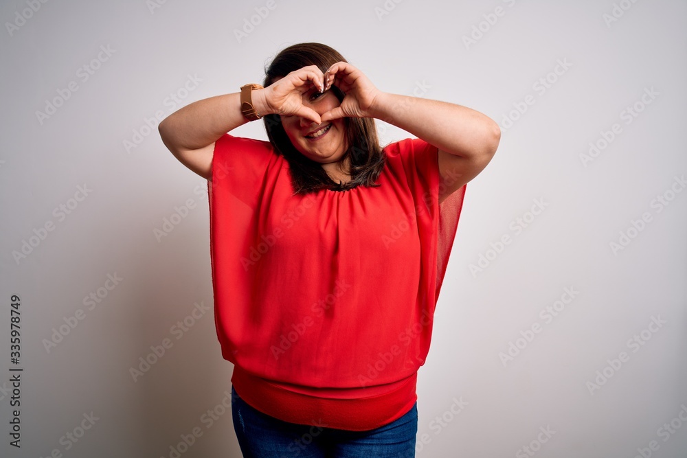 Beautiful brunette plus size woman wearing casual red t-shirt over isolated white background Doing heart shape with hand and fingers smiling looking through sign Beautiful brunette plus size woman wearing casual red t-shirt over isolated white background Doing heart shape with hand and fingers smiling looking through sign