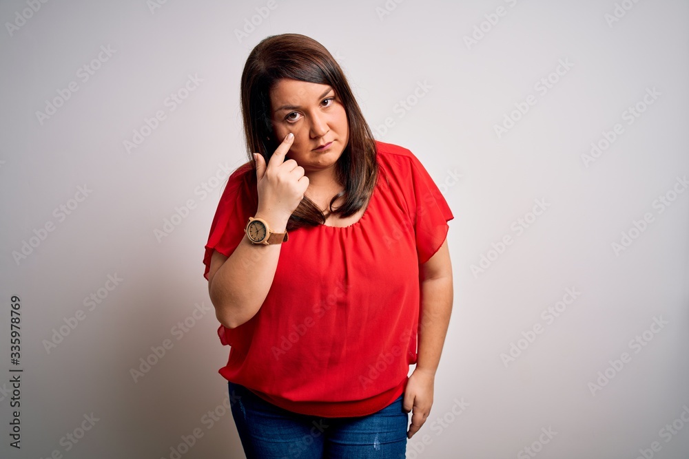 Beautiful brunette plus size woman wearing casual red t-shirt over isolated white background Pointing to the eye watching you gesture, suspicious expression Beautiful brunette plus size woman wearing casual red t-shirt over isolated white background Pointing to the eye watching you gesture, suspicious expression