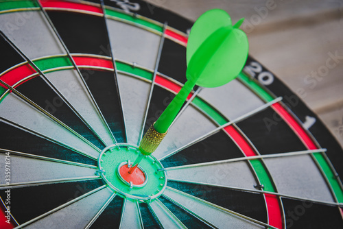 Close up shot of the green dart arrow hit on bull eyes of dartboard to represent that the business reached the target of company with Monochrome tone picture style. target and goal ass concept.