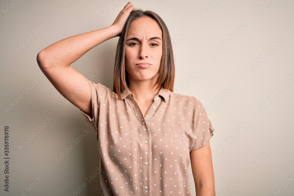 Young beautiful woman wearing casual shirt standing over isolated white background confuse and wonder about question. Uncertain with doubt, thinking with hand on head. Pensive concept. Young beautiful woman wearing casual shirt standing over isolated white background confuse and wonder about question. Uncertain with doubt, thinking with hand on head. Pensive concept.