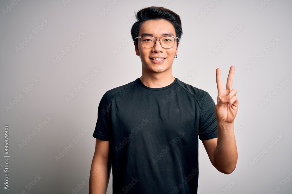 Young handsome chinese man wearing black t-shirt and glasses over white background showing and pointing up with fingers number two while smiling confident and happy. Young handsome chinese man wearing black t-shirt and glasses over white background showing and pointing up with fingers number two while smiling confident and happy.
