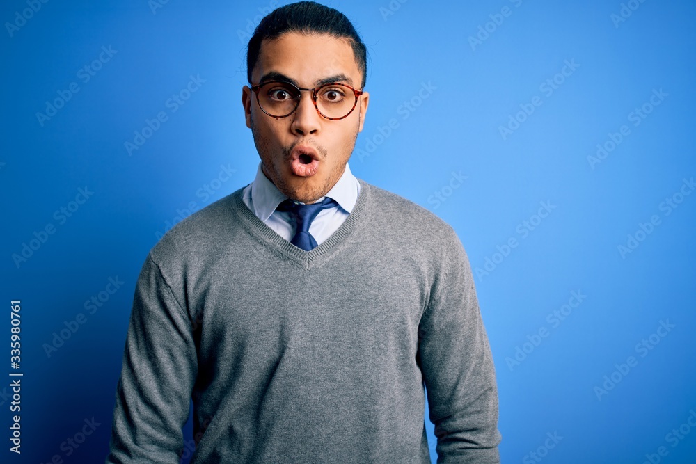 Young brazilian businessman wearing tie standing over isolated blue background afraid and shocked with surprise expression, fear and excited face. Young brazilian businessman wearing tie standing over isolated blue background afraid and shocked with surprise expression, fear and excited face.