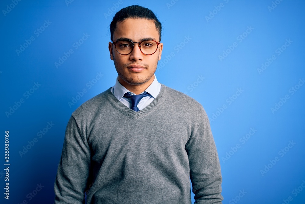 Young brazilian businessman wearing tie standing over isolated blue background with serious expression on face. Simple and natural looking at the camera. Young brazilian businessman wearing tie standing over isolated blue background with serious expression on face. Simple and natural looking at the camera.