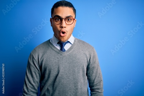 Young brazilian businessman wearing tie standing over isolated blue background afraid and shocked with surprise expression, fear and excited face. © Krakenimages.com